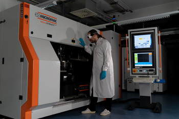 A scientist stands next to a laser system used for microstructuring flat and free-form surfaces using ultrashort laser pulses.